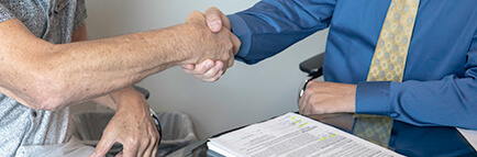 Two people shaking hands over contract on desk