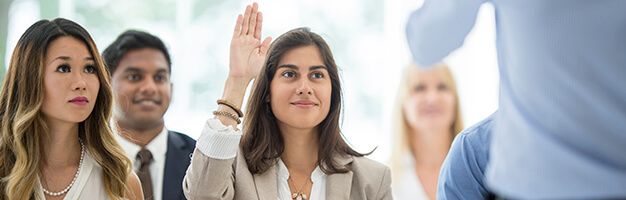 Woman in training group seated with hand raised to ask a question