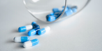 Multiple blue and white medication capsules spilling out of a clear class on a countertop